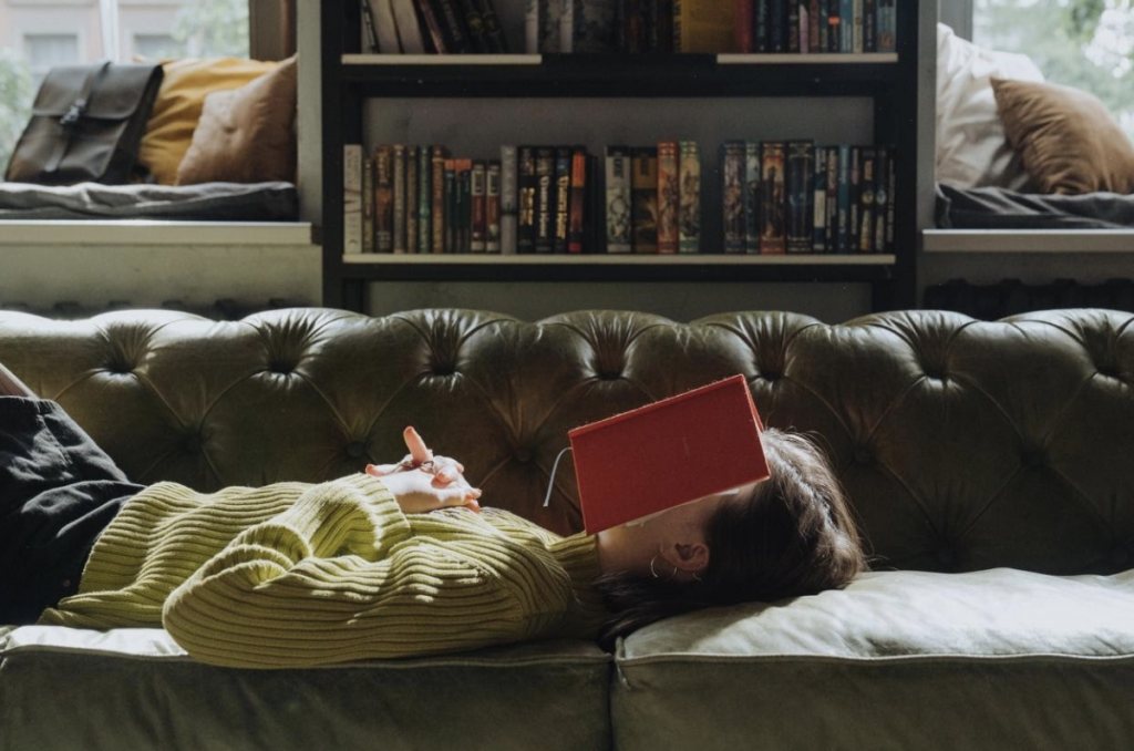 一位女生躺在沙發上用書蓋住頭