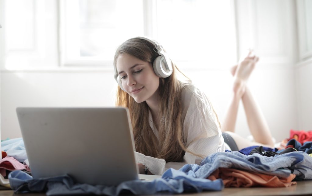 一個女生躺在床戴耳機愉快的用電腦